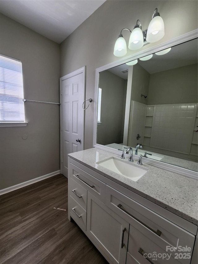 bathroom featuring a tile shower, vanity, baseboards, and wood finished floors