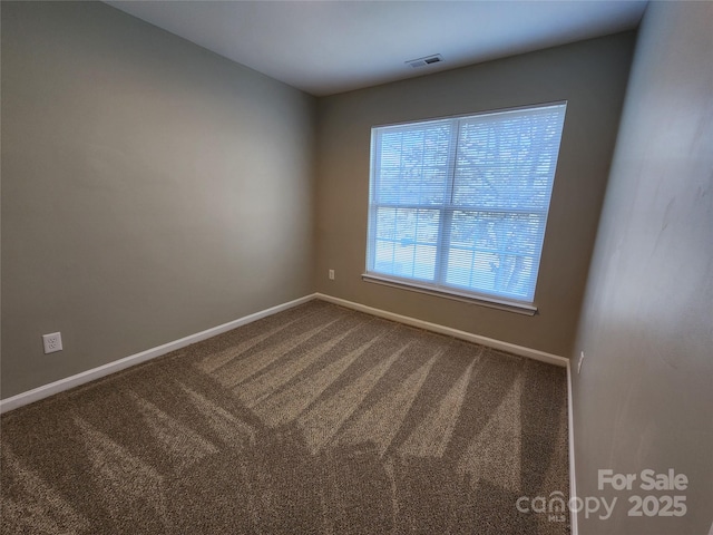 spare room featuring baseboards, visible vents, and dark colored carpet