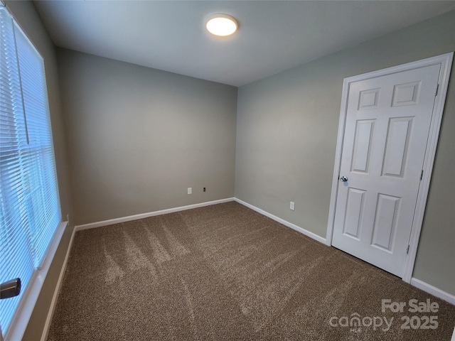 unfurnished room featuring baseboards and dark carpet