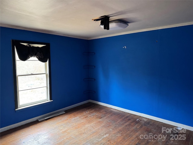 empty room with baseboards, wood-type flooring, and crown molding