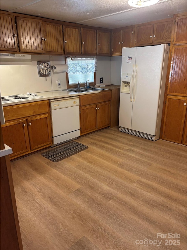 kitchen with light wood finished floors, white appliances, under cabinet range hood, and a sink