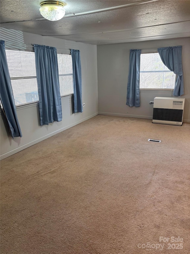 carpeted empty room with baseboards, heating unit, a textured ceiling, and a healthy amount of sunlight