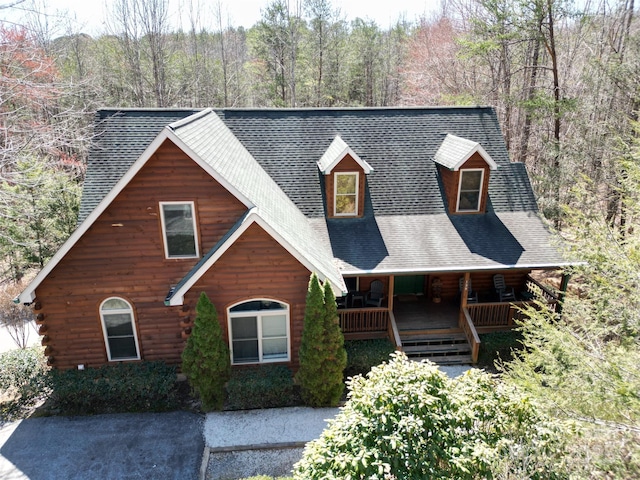 log cabin with a porch, log exterior, a wooded view, and a shingled roof