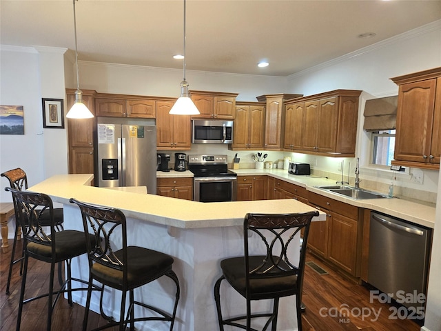 kitchen featuring dark wood-style flooring, a sink, ornamental molding, stainless steel appliances, and a kitchen bar