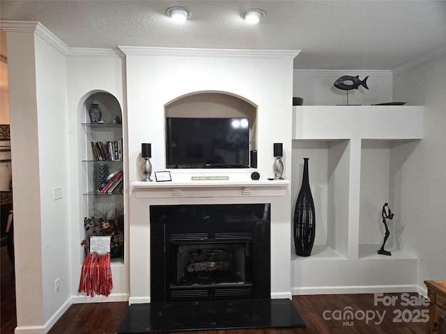 living room with built in shelves, wood finished floors, a fireplace with flush hearth, a textured ceiling, and crown molding