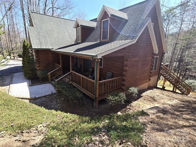 back of house with a porch, log exterior, and roof with shingles