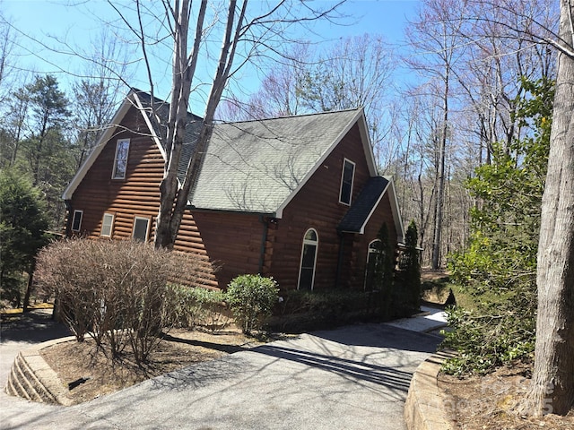 view of property exterior featuring aphalt driveway, roof with shingles, and log exterior