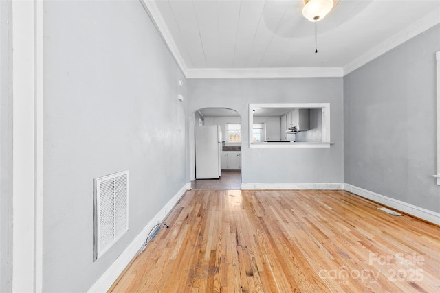 unfurnished living room featuring visible vents, baseboards, ornamental molding, wood finished floors, and arched walkways