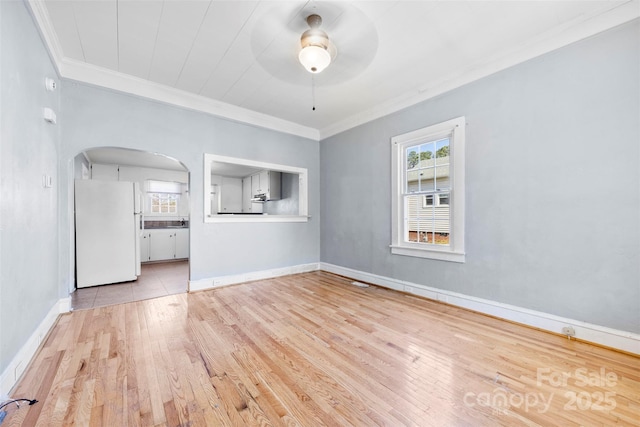 spare room with arched walkways, a healthy amount of sunlight, wood finished floors, and a ceiling fan