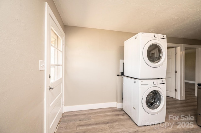 washroom featuring light wood-style floors, baseboards, stacked washing maching and dryer, and a textured ceiling