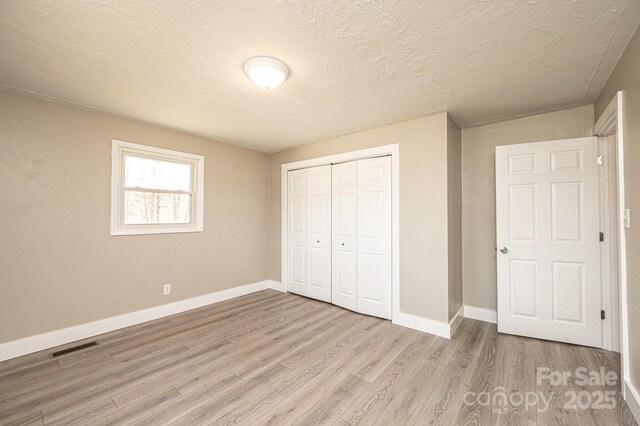unfurnished bedroom featuring a closet, baseboards, visible vents, and light wood finished floors
