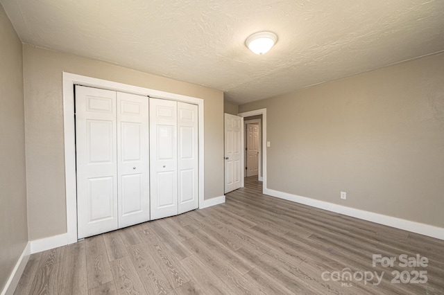 unfurnished bedroom with a closet, baseboards, a textured ceiling, and wood finished floors