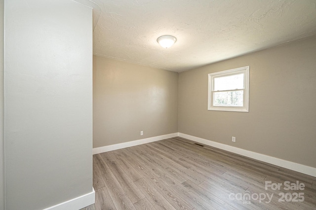 spare room featuring baseboards, a textured ceiling, and light wood finished floors