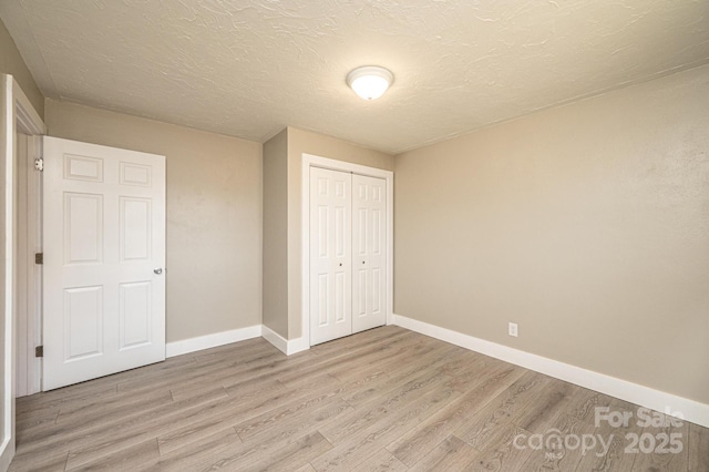 unfurnished bedroom featuring a closet, a textured ceiling, baseboards, and light wood finished floors