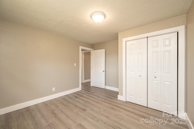 unfurnished bedroom featuring baseboards, a closet, light wood-style floors, and a textured ceiling