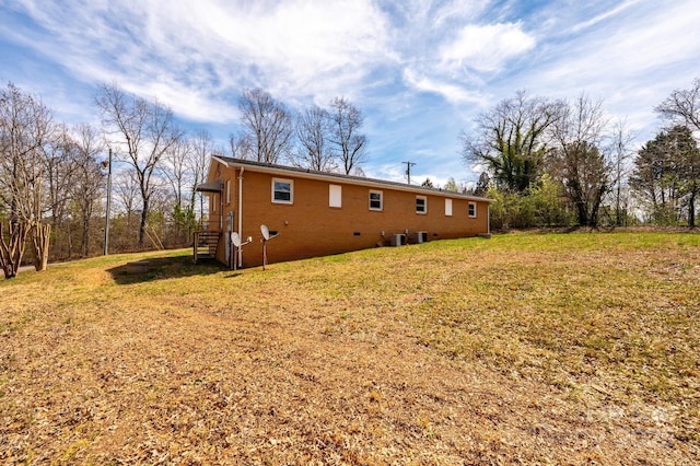 rear view of house featuring brick siding, central AC, and a lawn