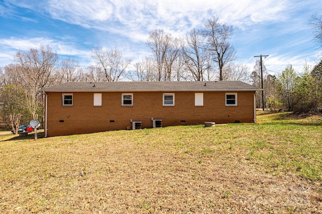 back of property featuring brick siding, crawl space, central AC, and a yard