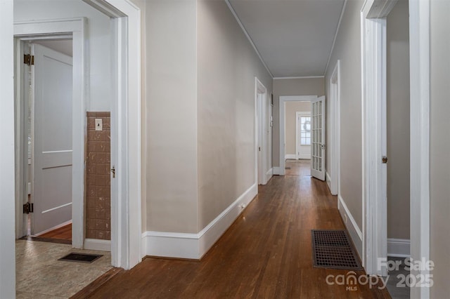 hallway featuring visible vents, baseboards, wood finished floors, and ornamental molding