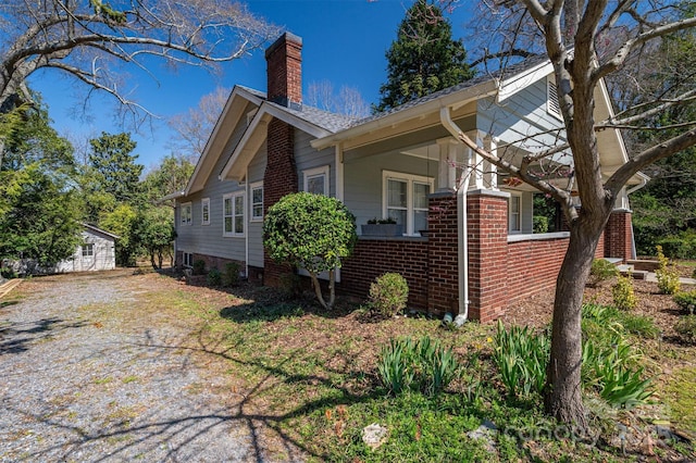 view of property exterior featuring an outbuilding, brick siding, driveway, and a chimney