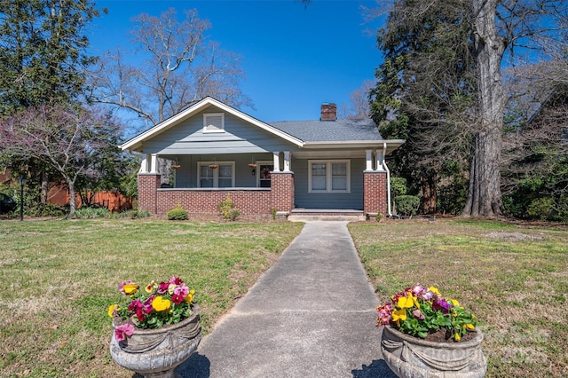 view of front of property with brick siding, covered porch, a chimney, and a front yard