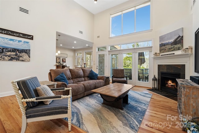 living area featuring a tiled fireplace, visible vents, baseboards, and wood finished floors