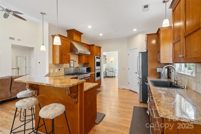 kitchen featuring stainless steel appliances, brown cabinets, a peninsula, and wall chimney range hood