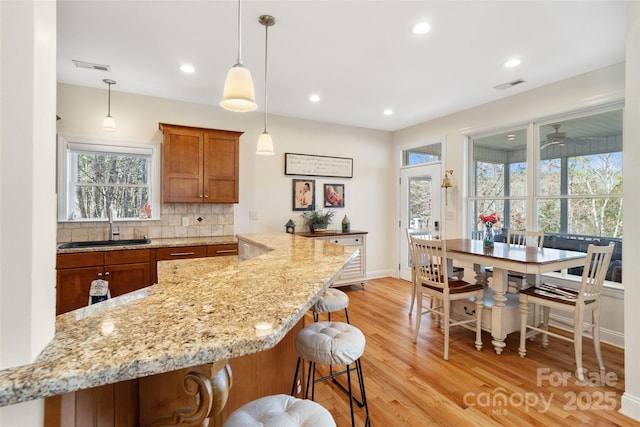 kitchen with brown cabinetry, visible vents, a sink, decorative backsplash, and light wood-style floors