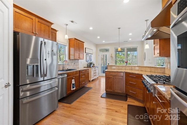 kitchen with ventilation hood, light wood-type flooring, brown cabinets, stainless steel appliances, and a sink