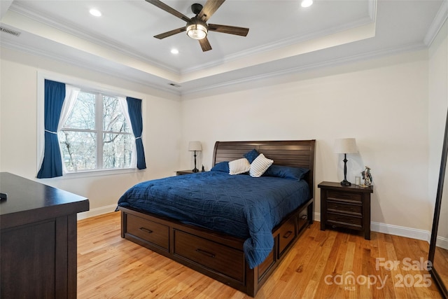 bedroom with a raised ceiling, light wood-style flooring, and ornamental molding