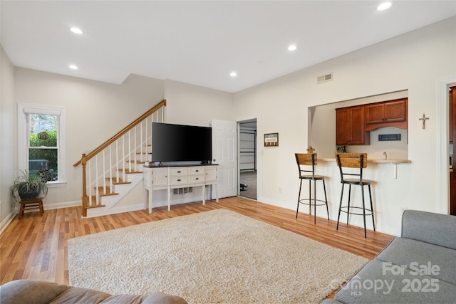 living area with light wood finished floors, visible vents, recessed lighting, and stairs