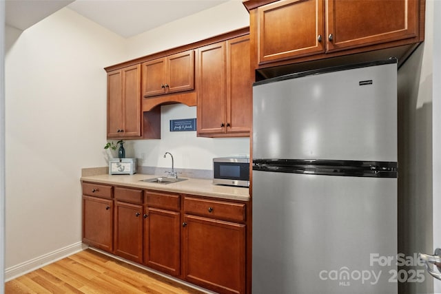 kitchen with light wood finished floors, light countertops, brown cabinetry, stainless steel appliances, and a sink