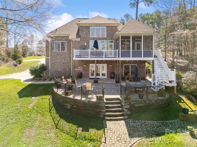 back of house with brick siding, a patio area, a yard, and a sunroom