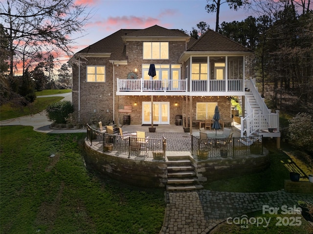 rear view of property featuring a lawn, stairway, a sunroom, brick siding, and a patio area