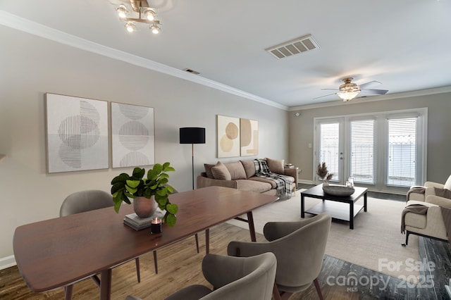 living area with visible vents, baseboards, wood finished floors, and crown molding