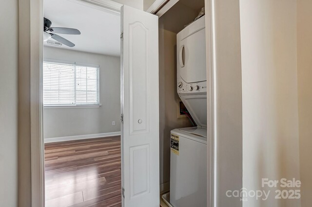 laundry room featuring baseboards, laundry area, wood finished floors, stacked washer / drying machine, and a ceiling fan