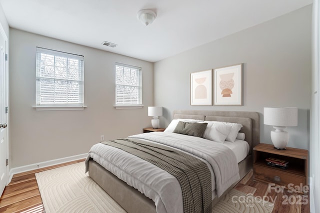 bedroom with visible vents, wood finished floors, and baseboards