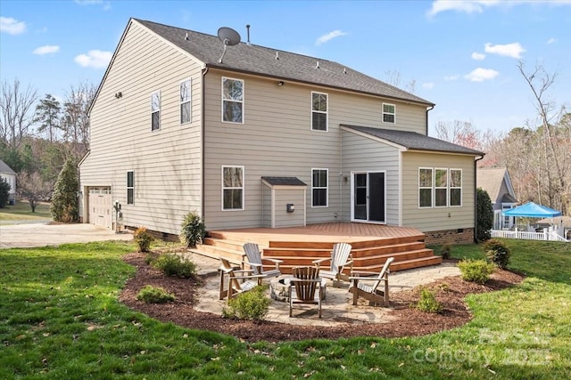 back of house with driveway, a wooden deck, an outdoor fire pit, a patio area, and a lawn