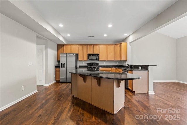 kitchen with a peninsula, recessed lighting, black appliances, dark wood-type flooring, and a kitchen breakfast bar