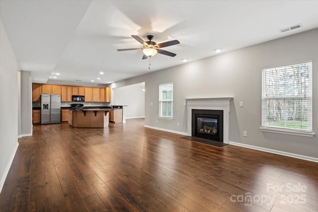 unfurnished living room featuring visible vents, a ceiling fan, dark wood-type flooring, and baseboards