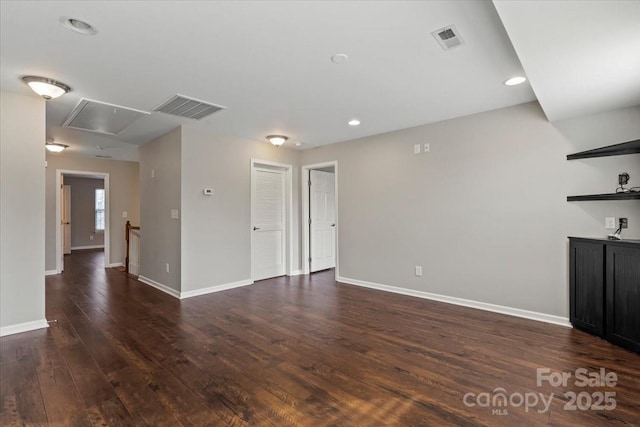 unfurnished living room featuring dark wood-style floors, visible vents, attic access, and baseboards