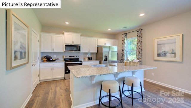 kitchen featuring a breakfast bar, a sink, backsplash, stainless steel appliances, and white cabinets