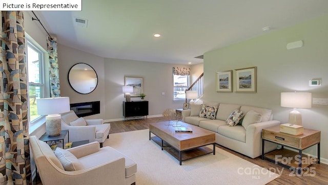 living area with visible vents, wood finished floors, a glass covered fireplace, and stairway