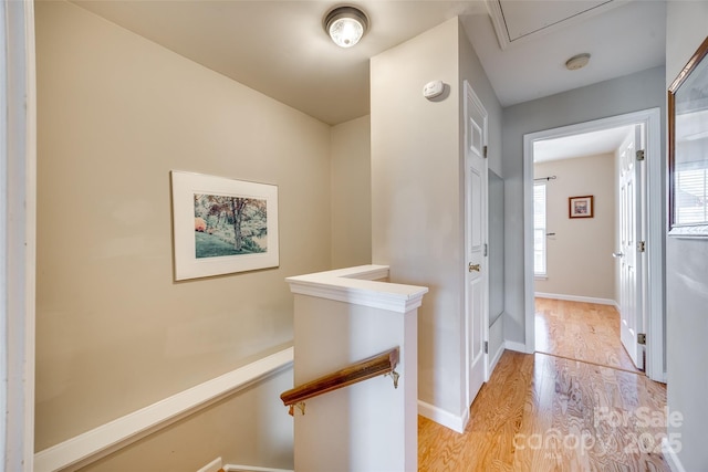 hall with an upstairs landing, attic access, light wood-type flooring, and baseboards