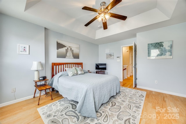 bedroom featuring baseboards, a raised ceiling, and light wood-style flooring