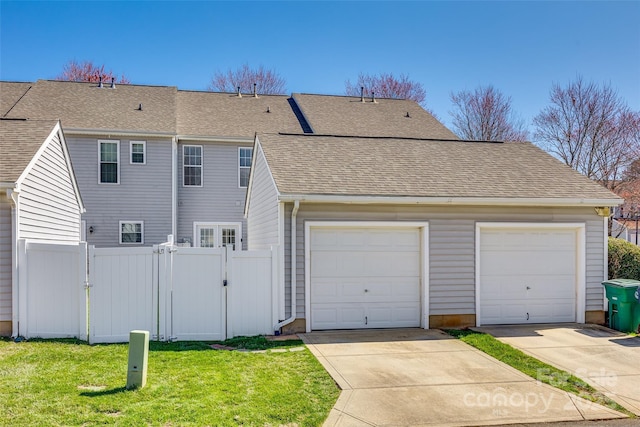 back of house featuring a shingled roof, fence, a lawn, a garage, and a gate