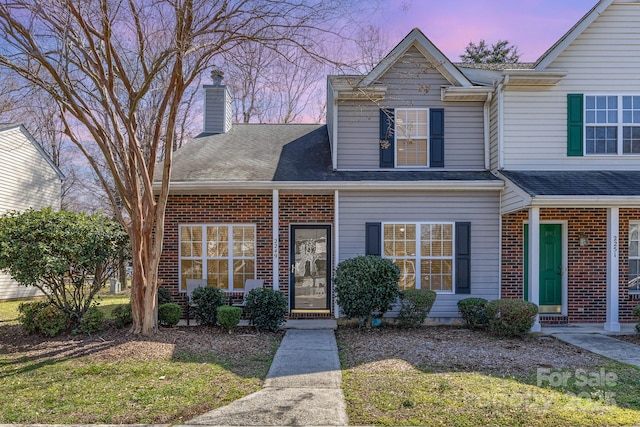 view of front of house featuring brick siding, a chimney, and roof with shingles