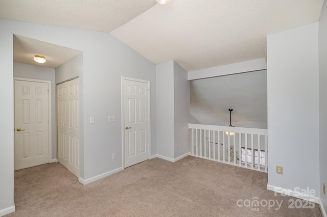 carpeted empty room featuring baseboards and vaulted ceiling