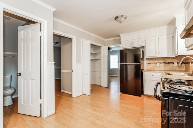 kitchen with a sink, black appliances, light countertops, white cabinetry, and crown molding