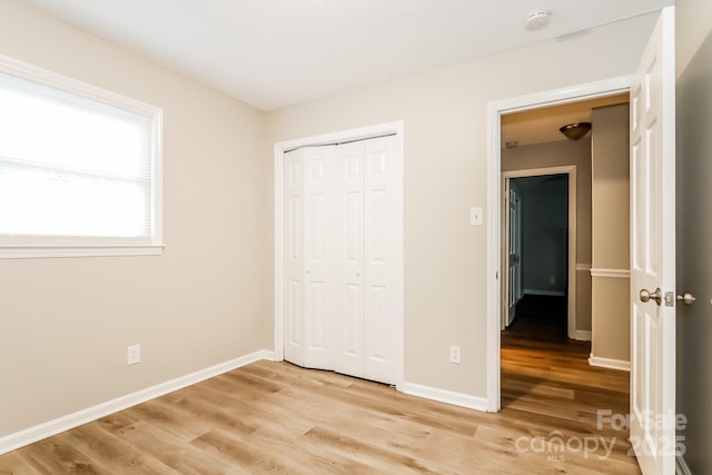 unfurnished bedroom featuring baseboards, light wood-type flooring, and a closet