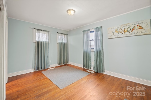 spare room with crown molding, baseboards, and wood-type flooring